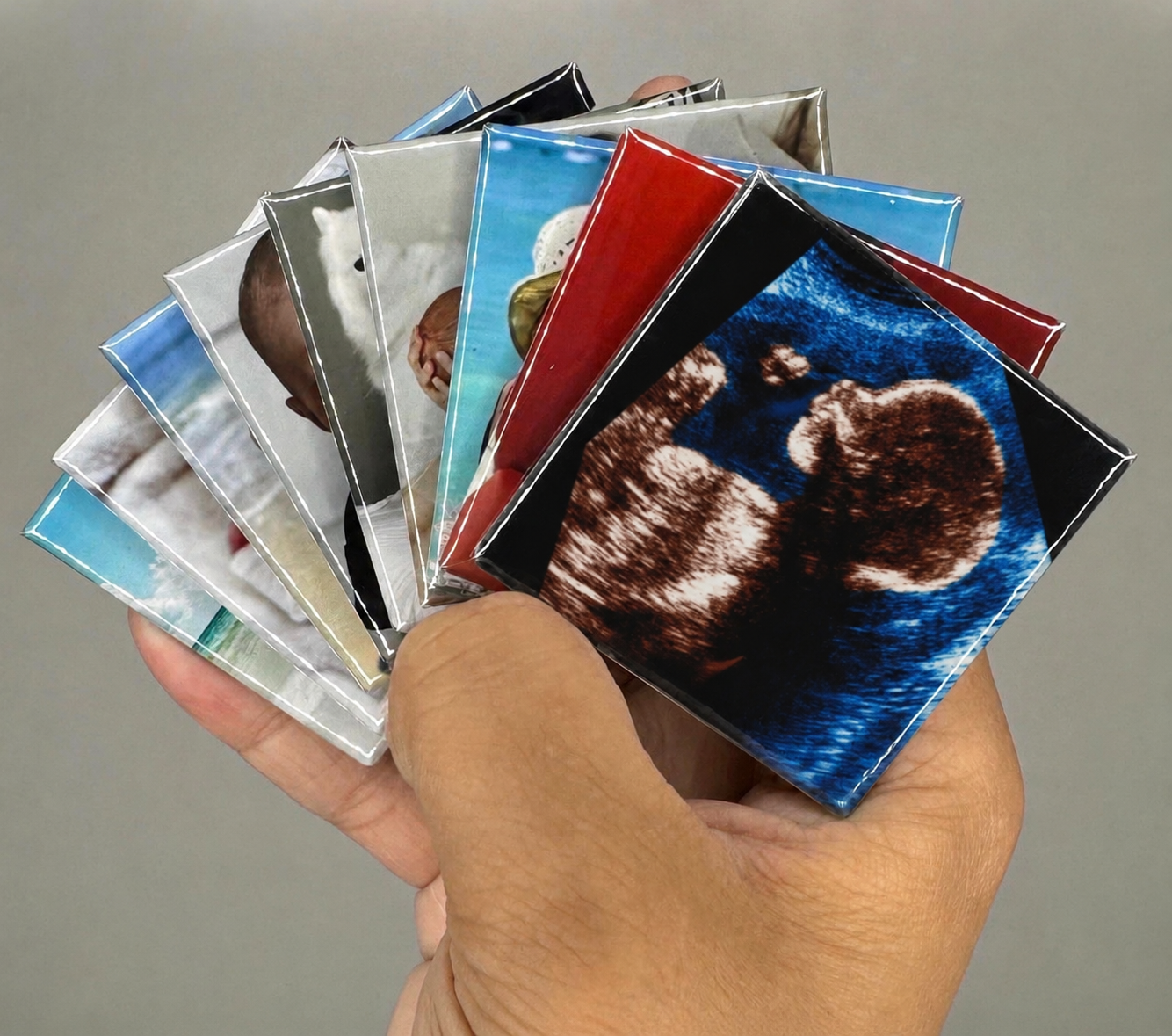 Hand holding a fan of custom fridge picture magnets with an ultrasound print on top